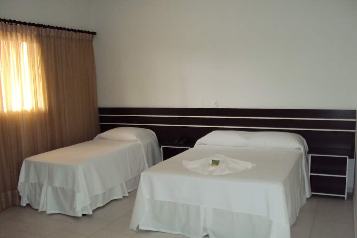 Una habitación de hotel con dos camas individuales, un ventanal con cortinas y una pared blanca lisa.