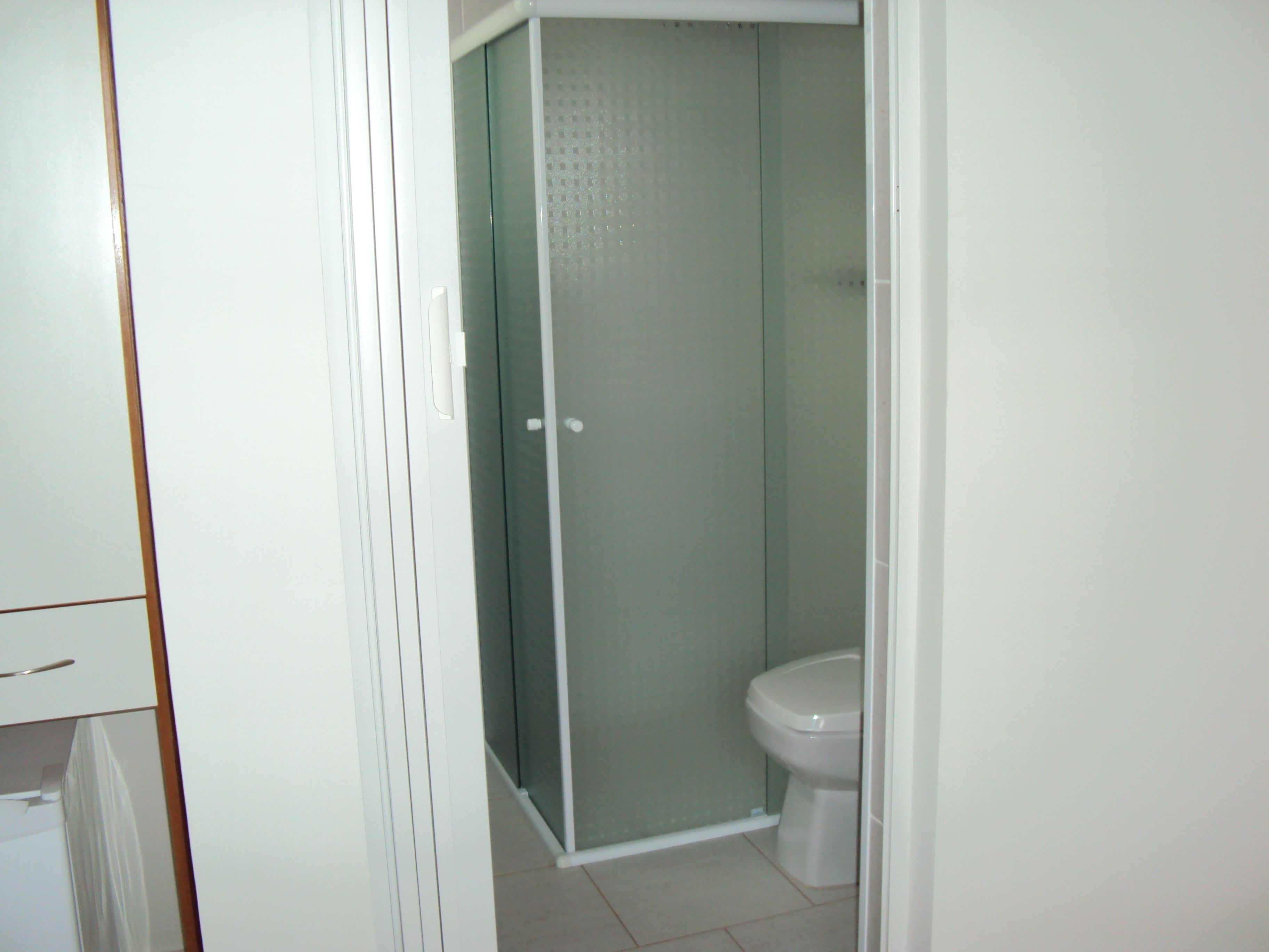 Een badkamer met toilet, douchecabine en een wit kastje.