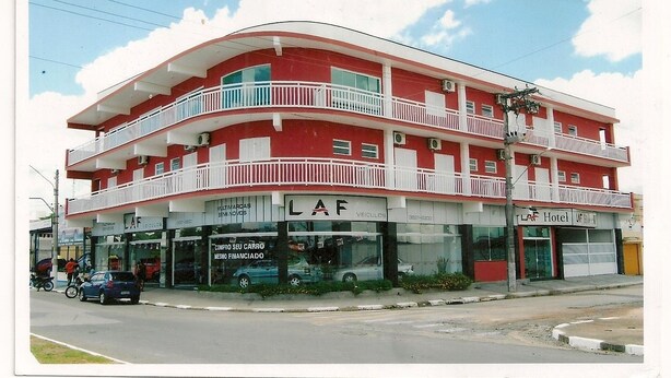 A multi-story building with a red facade, balconies, and storefronts including a car dealership and a hotel. - Laf Hotel (Registro)