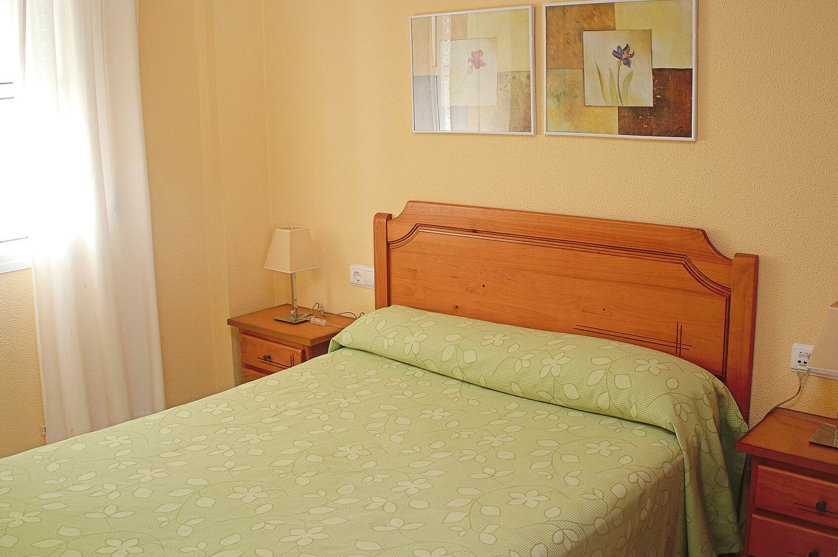 A bedroom with a wooden bed, a nightstand with a lamp, and two framed pictures on the wall.