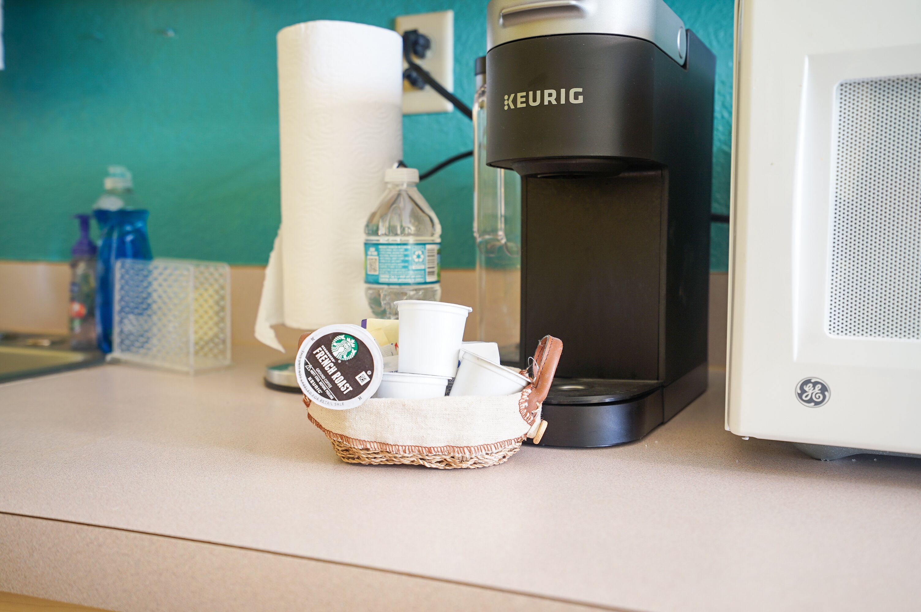Une machine à café, un panier rempli de tasses à café et une bouteille d’eau sont posés sur un comptoir.