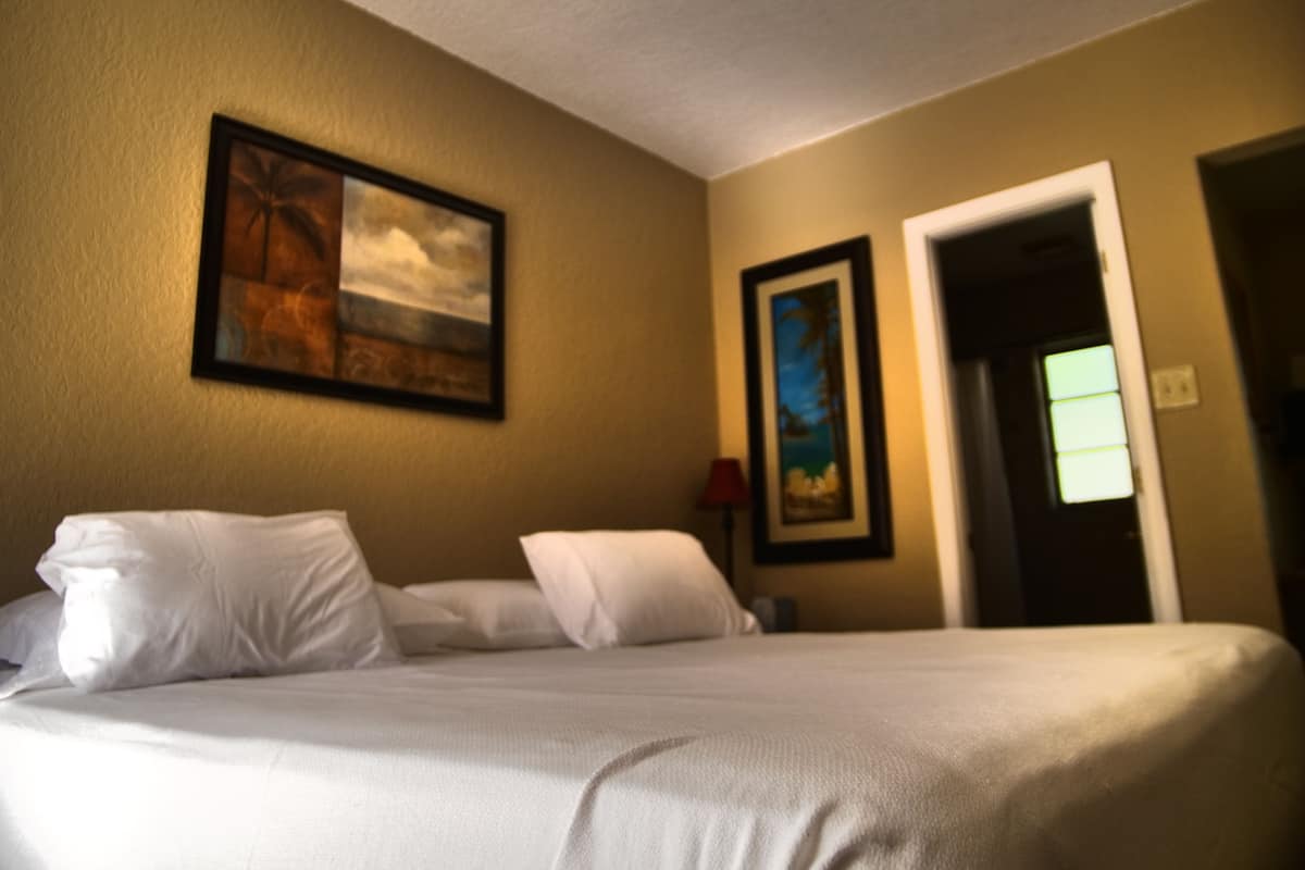 Una habitación de hotel con una cama, dos cuadros en la pared y una puerta que da a otra habitación.