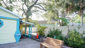 Un patio con un banco de madera, una zona de estar cubierta y un edificio con detalles azules.