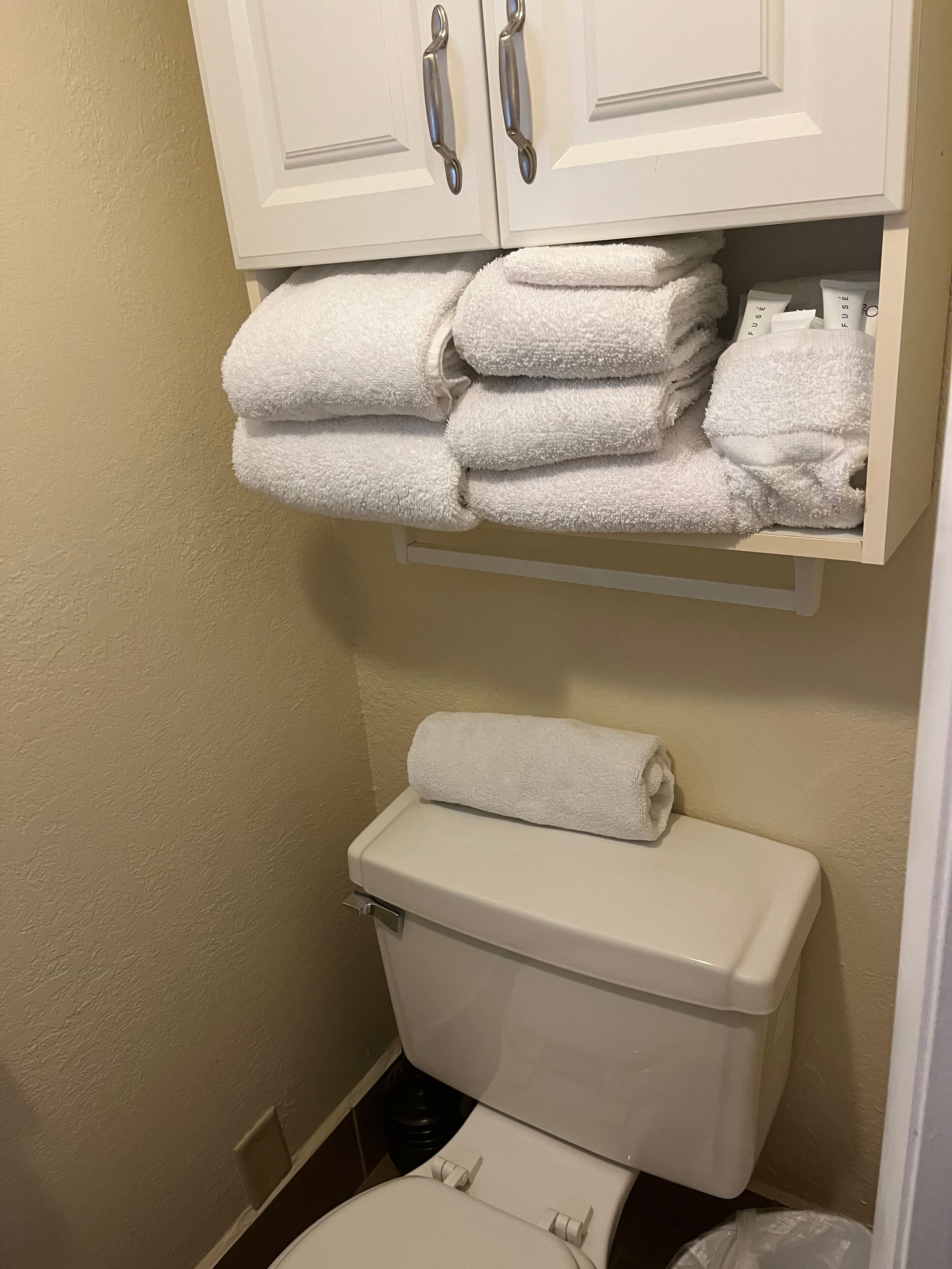 Un baño con inodoro, toallero con toallas dobladas y un mueble sobre el inodoro.