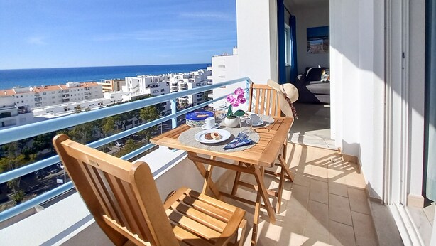 Un balcon avec une table en bois, dressée pour deux personnes, d’où l’on peut admirer le paysage urbain et la mer.