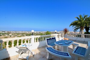 Una terraza con barandilla blanca, una mesa con sillas de azulejos azules y vistas a la ciudad y al mar.