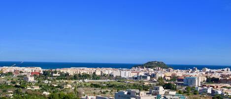 A coastal cityscape with a mix of residential and commercial buildings, a prominent hill, and a clear blue sky.