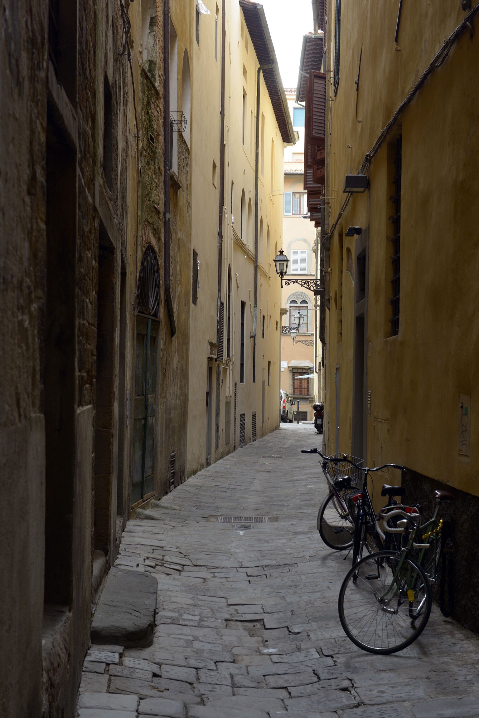A narrow cobblestone street flanked by historic buildings with balconies and a bicycle parked on the right.