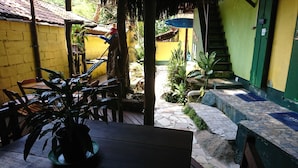 A courtyard with a wooden table and chairs, potted plants, a staircase, and a yellow wall. - Bela Casa Ilha Grande (Angra dos Reis)