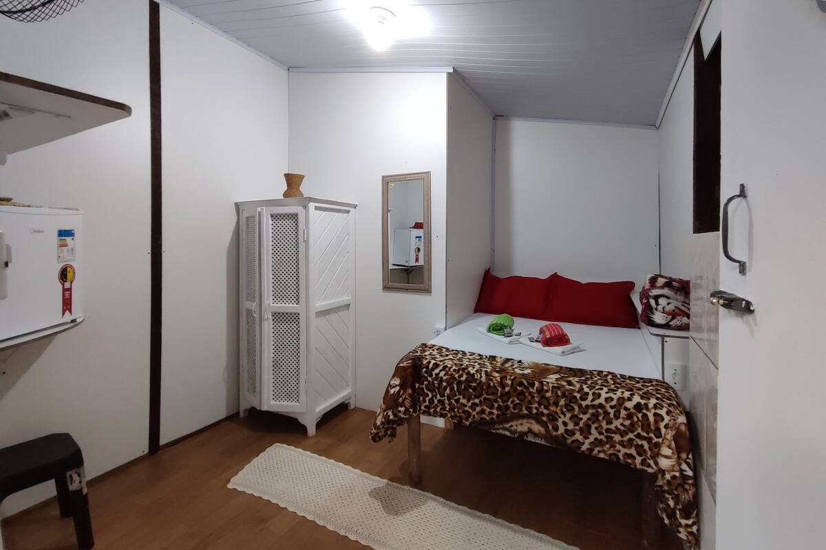 A small, clean room with a bed, a heater, a mirror, and a small table.