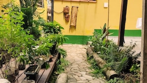 A stone pathway leading to a yellow building with a green base, surrounded by lush greenery and potted plants. - Bela Casa Ilha Grande (Angra dos Reis)