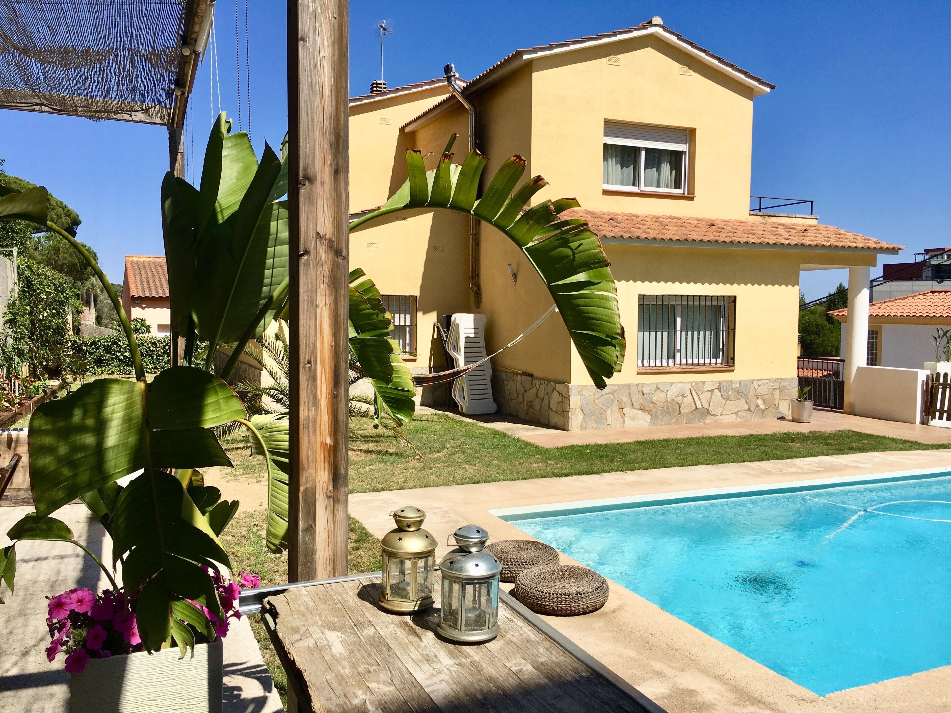 A house with a swimming pool, surrounded by greenery and a clear sky.