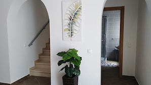 Un passadís amb una escala, una planta gran en test i una obra d'art emmarcada a la paret.
