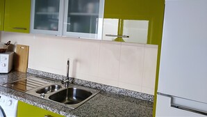 Una cocina con gabinetes verdes, un lavamanos de acero inoxidable y un refrigerador blanco.