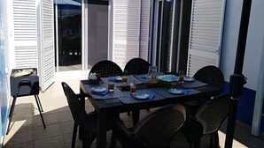 Zona d'aigüabarreig exterior amb taula preparada per a quatre persones, rodejada de cadires, sota un told blau.