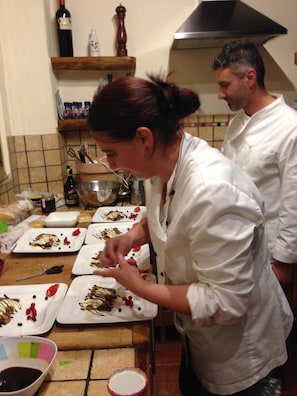 A kitchen with chefs preparing food, a tiled backsplash, and various cooking utensils and ingredients on the counter. - Luxury Villa, Private Pool, Views, Barga, Tuscany. 3 ensuite Bedrooms  (Barga)