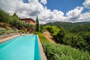 Une piscine avec vue sur une colline et un bâtiment rouge en arrière-plan.