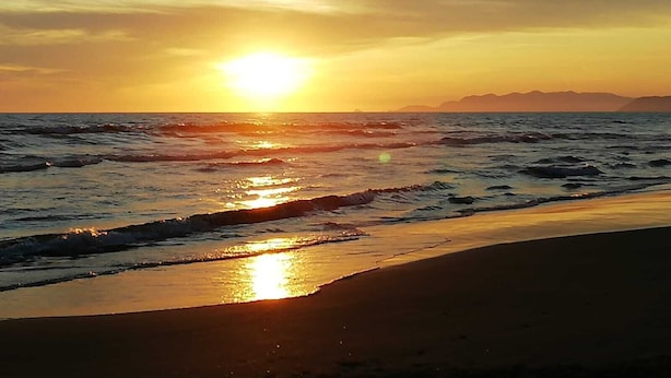 A beach scene with the sun setting over the ocean, waves gently lapping the shore.