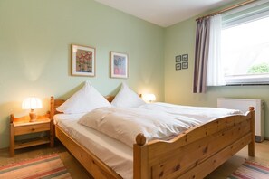 Un lit simple avec un cadre en bois, deux tables de chevet avec des lampes et une fenêtre avec des rideaux.