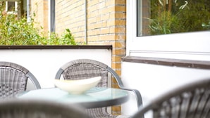 An outdoor seating area with wicker chairs and a glass table, featuring a brick wall and greenery in the background.