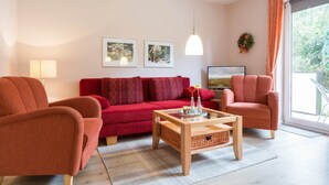 A modern living room with a red sofa, two armchairs, a wooden coffee table, and a TV.