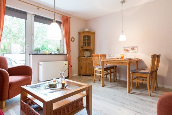 Une pièce chaleureuse comprenant une table à manger, des chaises, un buffet en bois et une fenêtre avec des rideaux.