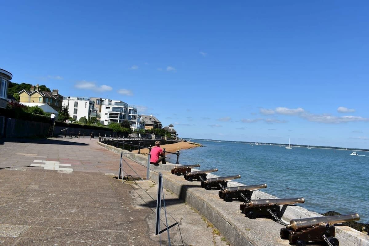 A waterfront promenade with a row of cannons, a clear sky, and buildings in the background.