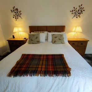 A neatly made bed with a plaid throw blanket, two bedside lamps, and decorative wall art. - OLD SMIDDY APARTMENT, BALLOCH, LOCH LOMOND SLEEPS 3 IN FAMILY ROOM (Balloch)