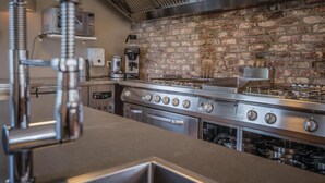 A commercial kitchen with stainless steel appliances, a brick wall, and a coffee machine.
