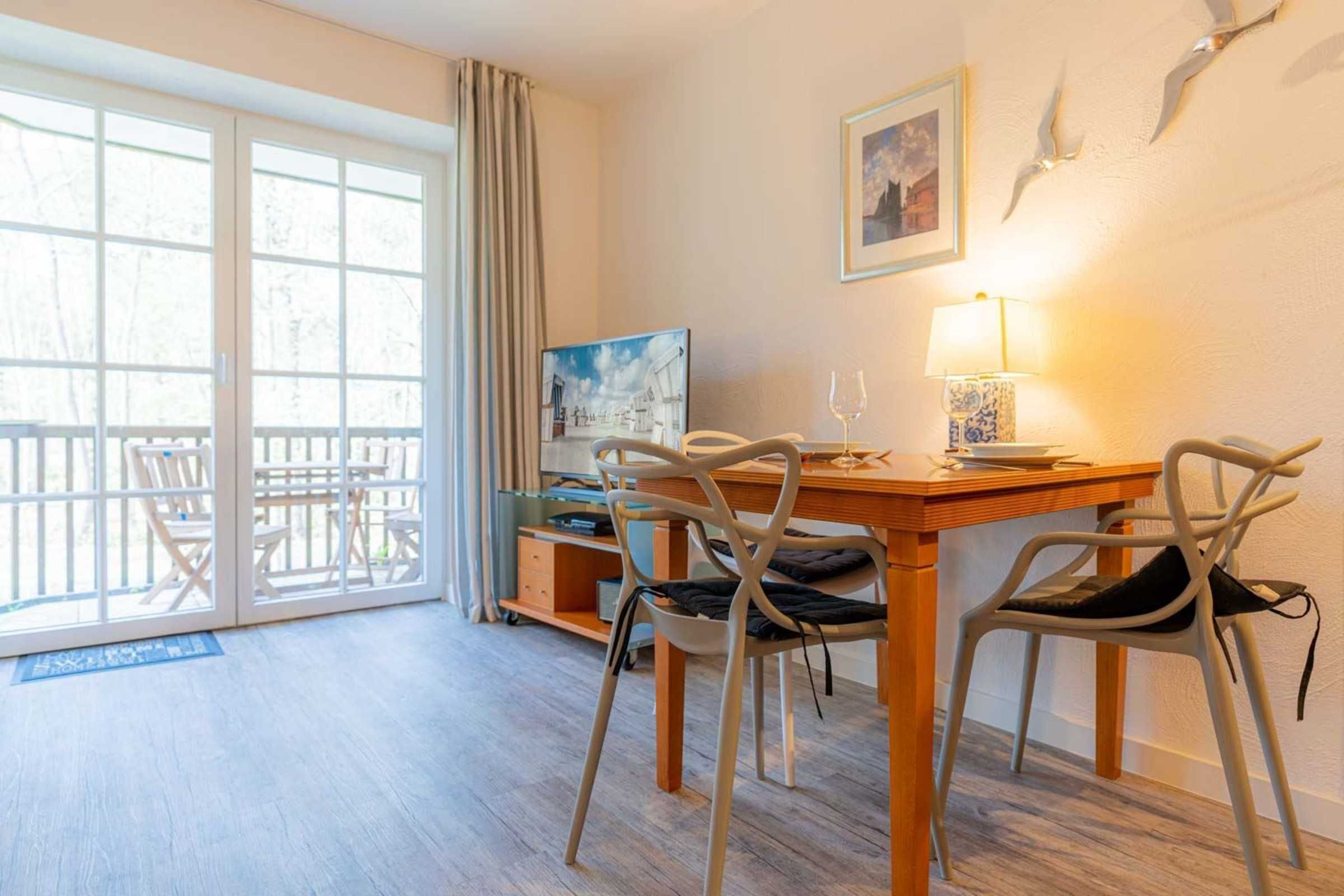 A dining area with a wooden table, two chairs, a television, and a lamp.