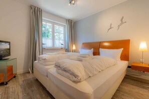 Habitación de hotel con una cama grande, dos mesitas de noche, un televisor sobre un mueble bajo y una ventana con cortinas.