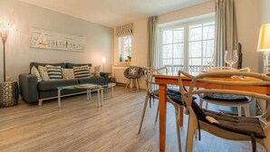A modern living room with a sofa, coffee table, and dining area with chairs and a table. - Apartment "Flounder" (ID 344) - Friesenresidence (Sankt Peter-Ording)