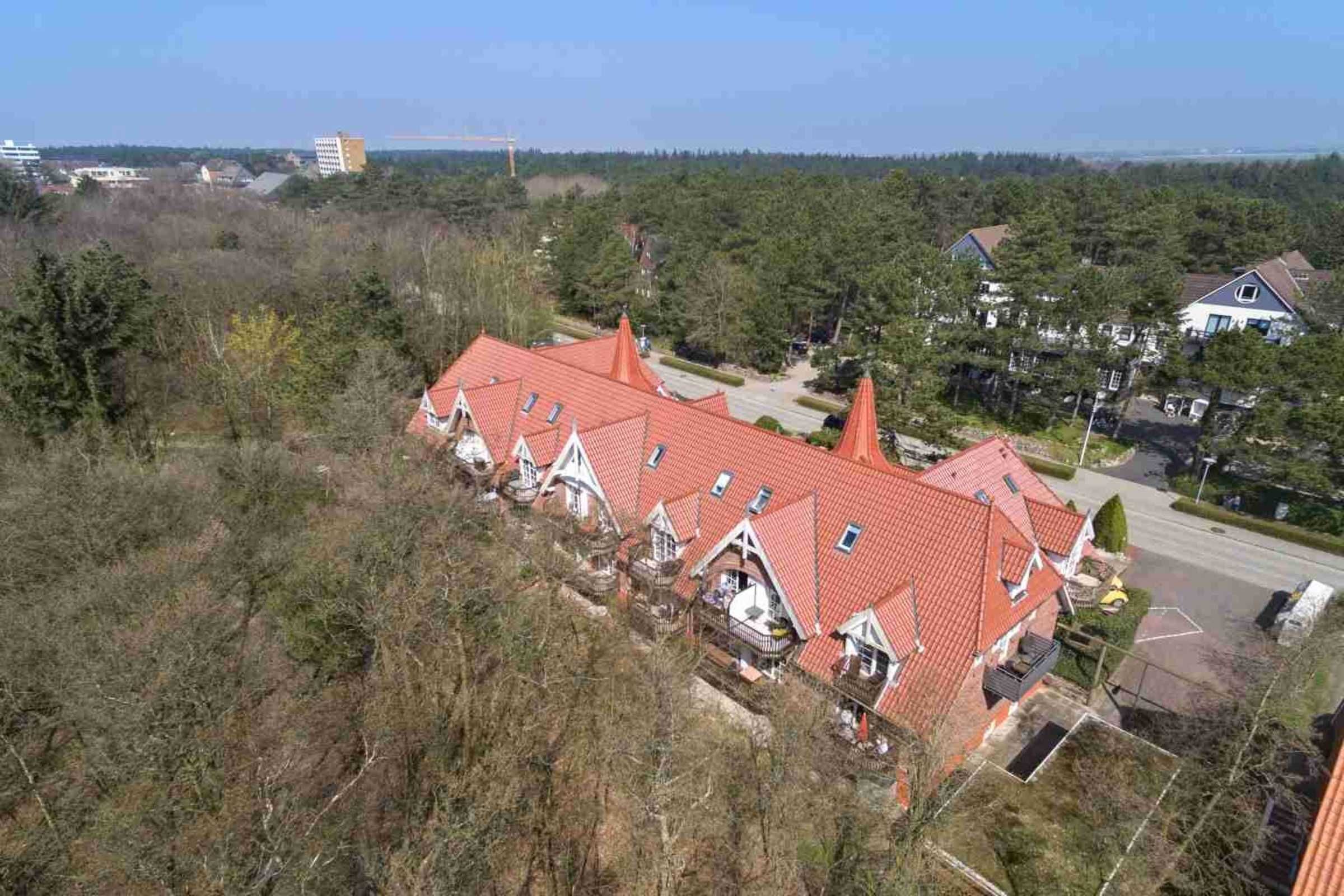 A row of houses with red roofs and white walls, surrounded by trees and a clear sky.