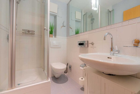 A modern bathroom with a glass-enclosed shower, a white toilet, and a large sink with a mirror above it. - Apartment "Flounder" (ID 344) - Friesenresidence (Sankt Peter-Ording)
