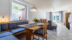 A dining area with a wooden table, blue upholstered benches, and a hanging light fixture. - Apartment 4 (ID 036), Germany (Sankt Peter-Ording)