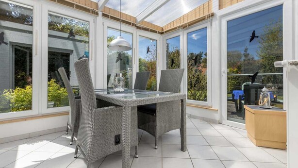 A sunroom with a glass table and wicker chairs, large windows, and a view of the garden. - Apartment 4 (ID 036), Germany (Sankt Peter-Ording)