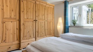 A bedroom with a large bed, wooden wardrobe, and a window with a view of greenery. - Apartment 4 (ID 036), Germany (Sankt Peter-Ording)