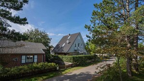 Un quartier résidentiel avec une maison dotée d’un toit en pente, d’une antenne parabolique bien visible et d’une allée pavée.