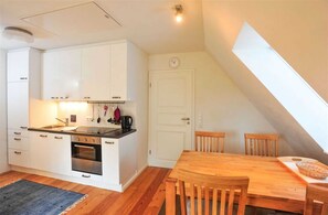 A compact kitchen with white cabinets, a wooden dining table, and a small oven. - Apartment OG Seute Deern (ID 029) (Sankt Peter-Ording)