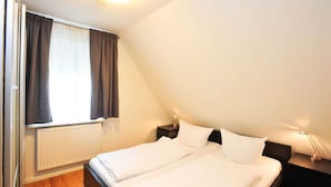 Une chambre à coucher avec un lit, deux tables de chevet, une fenêtre avec des rideaux et un radiateur.