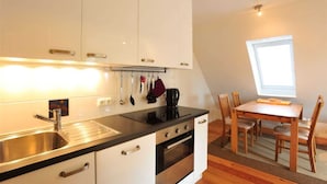 Une cuisine compacte avec des meubles blancs, un plan de travail noir et un coin repas comprenant des chaises et une table en bois.