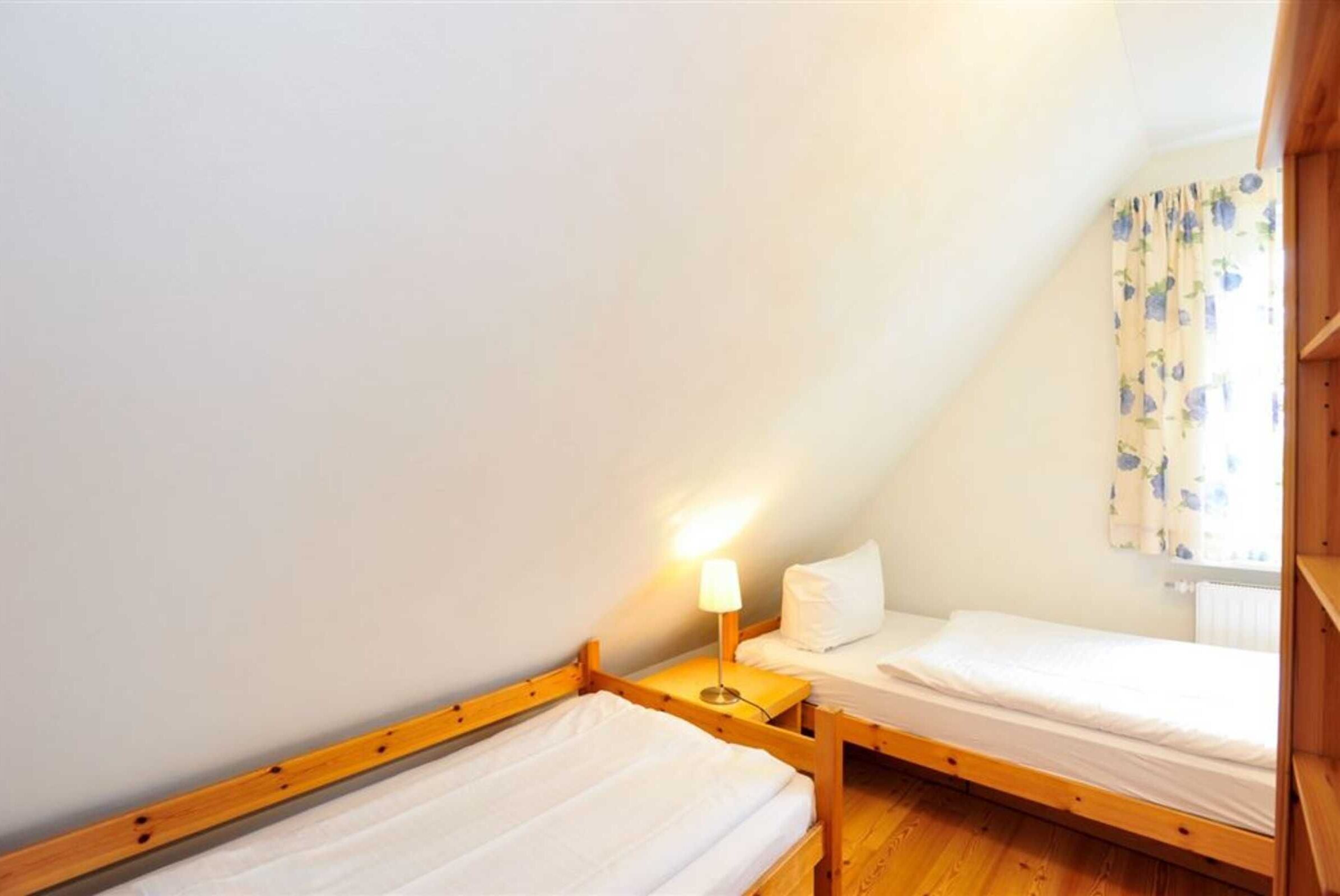 Ein kleiner, dreieckiger Raum mit zwei Holz-Etagenbetten, einem Nachttisch mit Lampe und einem Fenster mit blumigen Vorhängen.
