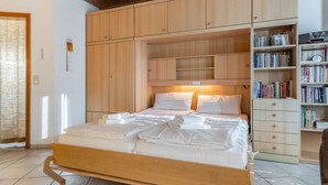 A bedroom with a wooden bed, a bookshelf, and a wooden wardrobe. - Apartment 23 (ID 031), Germany (Sankt Peter-Ording)