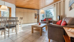 A spacious living area with a wooden ceiling, a dining table with chairs, a sofa, and a coffee table. - Apartment 23 (ID 031), Germany (Sankt Peter-Ording)