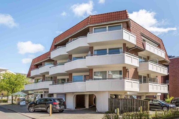 Un immeuble résidentiel à plusieurs étages, doté d’un toit recouvert de tuiles rouges, de murs extérieurs blancs et de balcons.