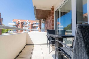 Un balcon avec une table et des chaises, une porte vitrée et une vue sur les maisons voisines.