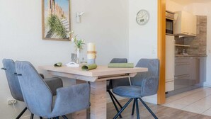 Un coin repas avec une table en bois, quatre chaises grises à revêtement rembourré, un vase avec des fleurs et une horloge au mur.