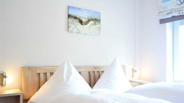 Un lit bien fait, avec du linge de lit blanc et une tête de lit en bois, dans une chambre d’hôtel.