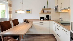 Une cuisine moderne avec des meubles blancs, une table à manger en bois et un four encastré.