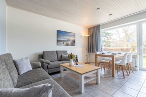 Uma sala de estar moderna com um sofá cinzento, uma mesa de centro de madeira e uma área de jantar com mesa e cadeiras.